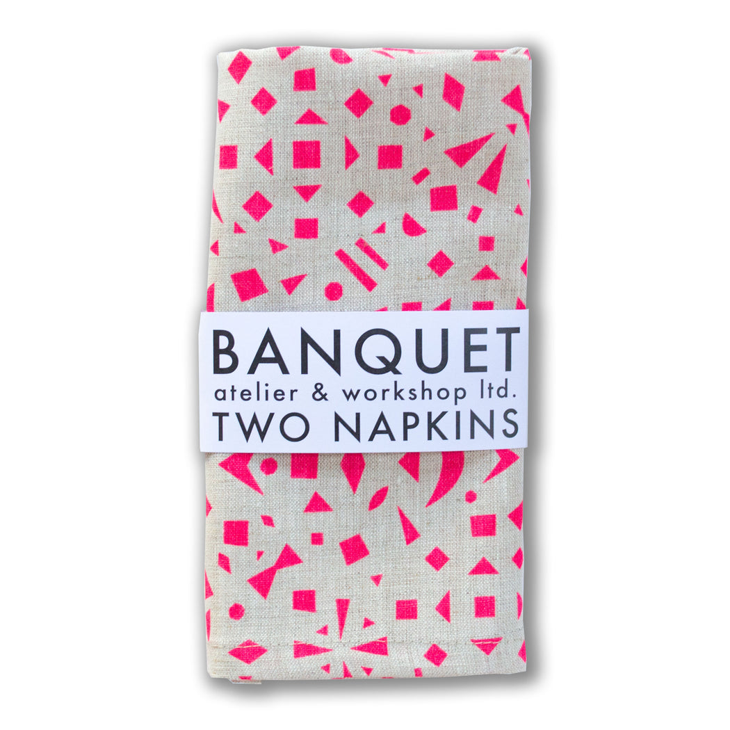 scattered neon pink shapes (triangles, squares, bow and trapezoids) on a pair of linen napkins